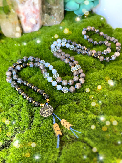 Blue Lotus Mala. 108 beads of Natural Opal, Chocolate Labradorite, Smokey Quartz, Blue Lace Agate, Clear Quartz, Brass spacers, Brass crescent moon spacers, and finished with a double sided Lotus and Ohm Charm.  Available at The Crystalline Moon.